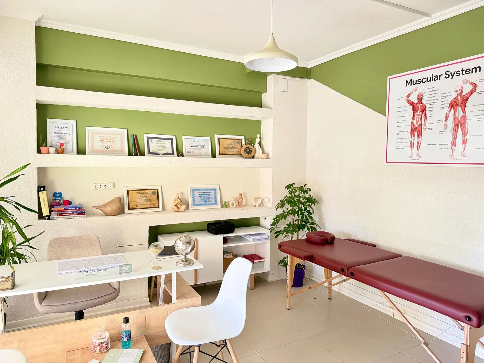 Elafiz Fizyoterapi'de görüşme masası, sertifikalar ve tedavi yatağının bulunduğu değerlendirme alanı